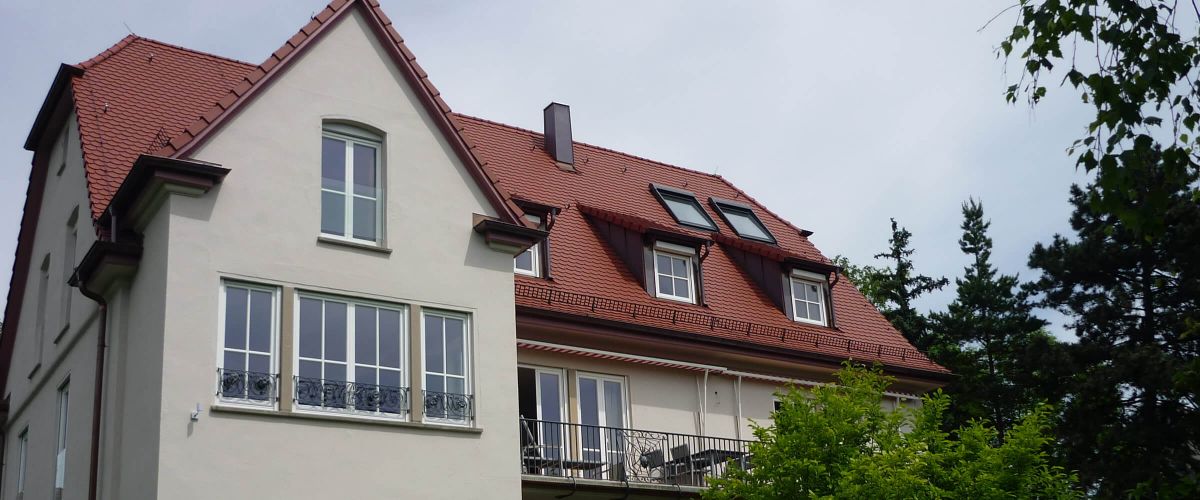 Komplettsanierung und Altbausanierung: Zweistöckiges Haus mit rotem Ziegeldach und ausgebautem Dachgeschoss