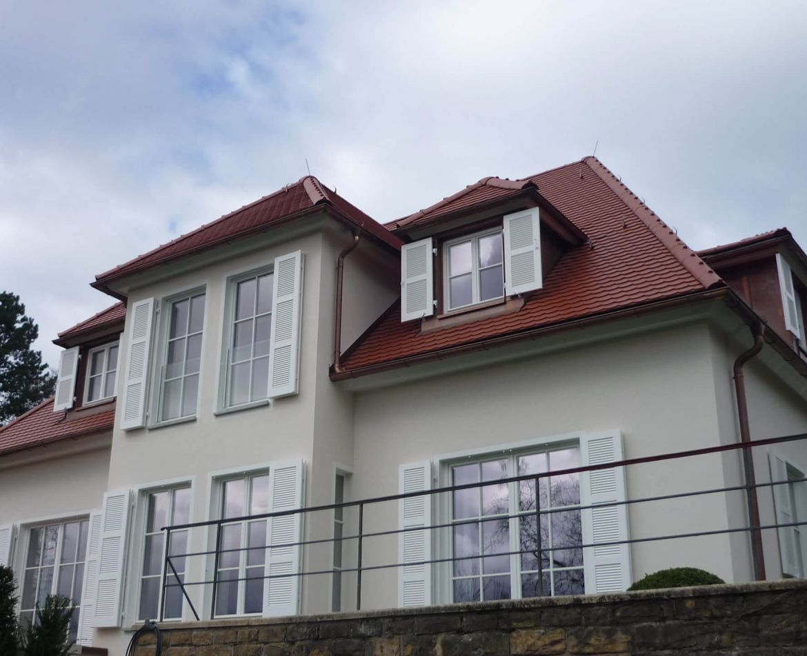 Renovierte Altbau-Fassade mit rotem Ziegeldach, weißen Fensterläden und einem umlaufenden Balkon