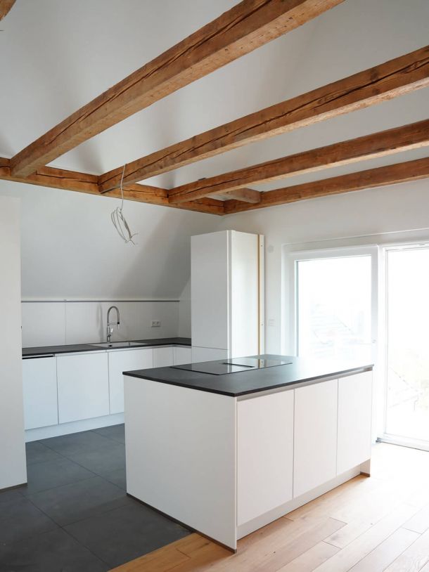 Sanierte Küche mit Kücheninsel und sichtbar integrierten Holzbalken aus Altbestand.
