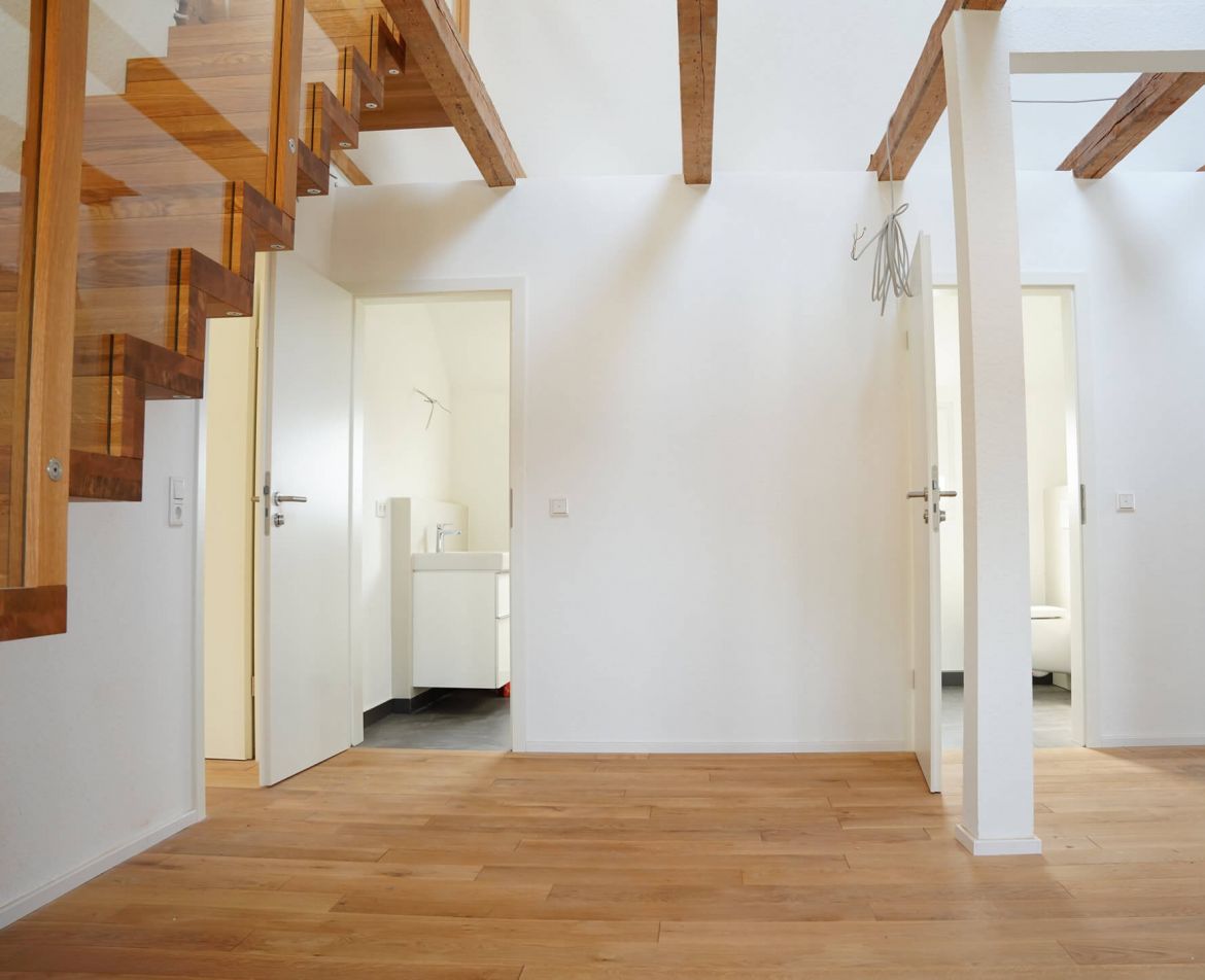 Treppenhaus mit Holzgeländer und verputzten Wänden nach der Altbausanierung in Stuttgart.